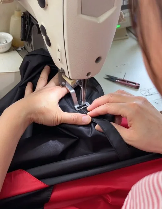 Hands guiding two-tone canopy panels through an industrial sewing machine
