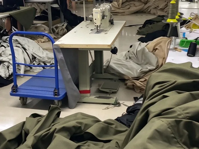 Sewing floor inside a partner workshop: industrial machines with panels and webbing under assembly